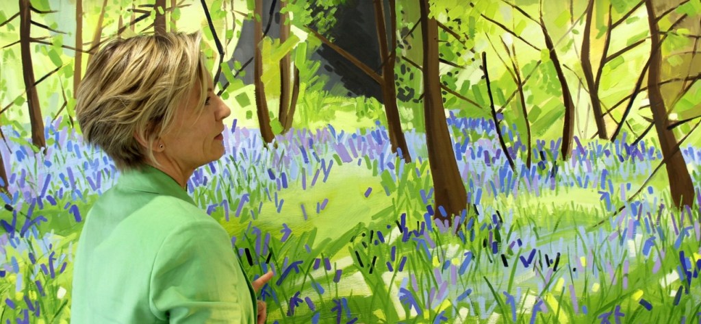 A woman in green looking at a colourful forest painting with blue flowers